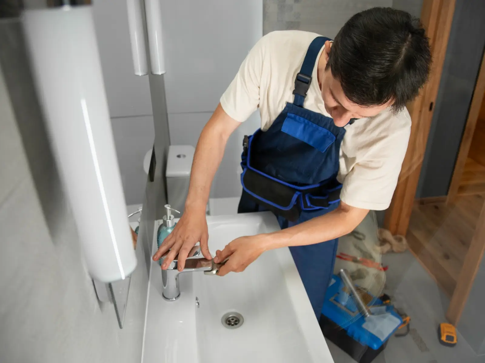 A person in a blue apron works on a modern sink faucet in a stylish bathroom, tools scattered on the floor A person in a blue apron works on a modern sink faucet in a stylish bathroom, tools scattered on the floor